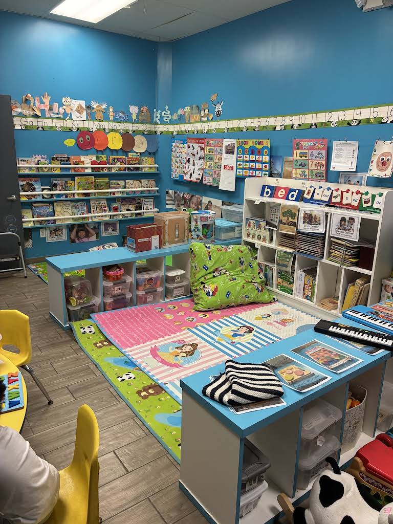 Bloom & Beyond's blue classroom with books, learning shelves, and a colorful play rug