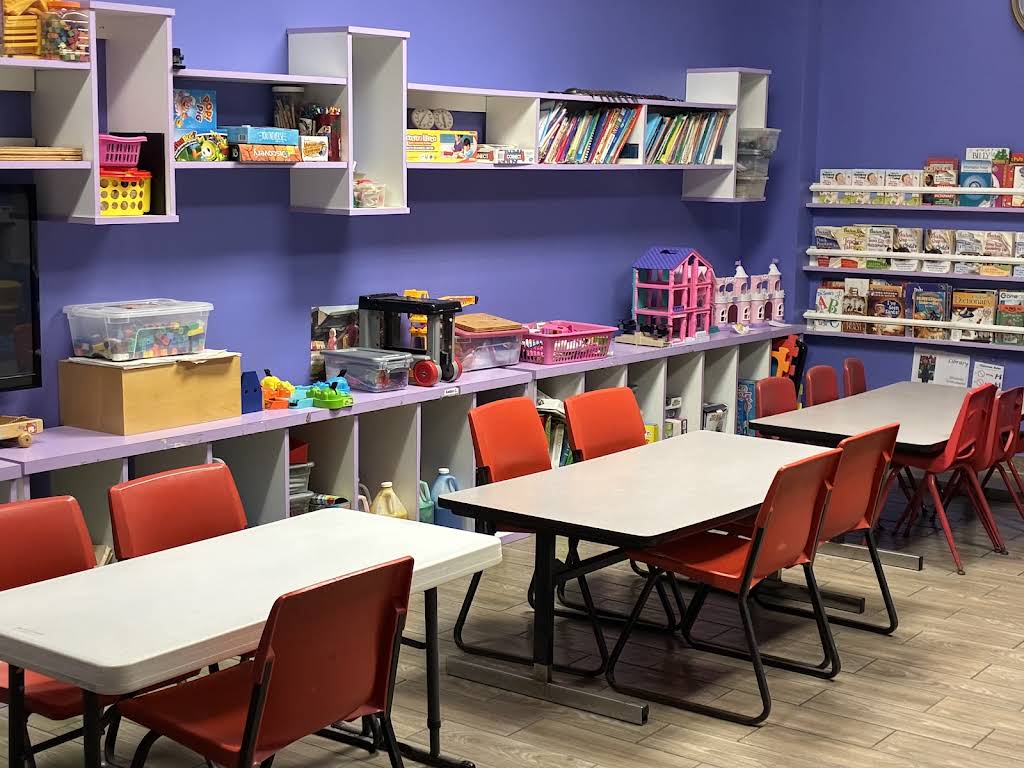 Bloom & Beyond's purple classroom with activity tables, red chairs, books, and toys